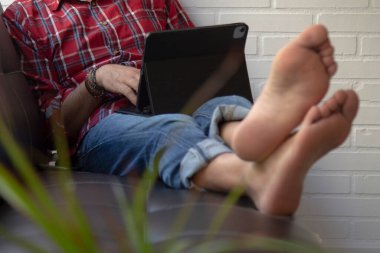 Tablet veya dizüstü bilgisayar kullanarak koltukta rahat bir adam.