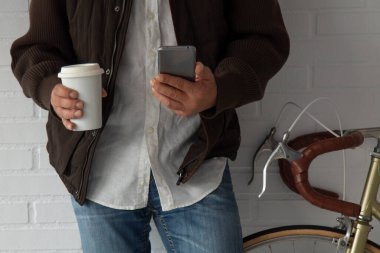 Bisikletin yanında ceketli ve cep telefonlu bir adam fotokopi alanı olan bir kahve içiyor.