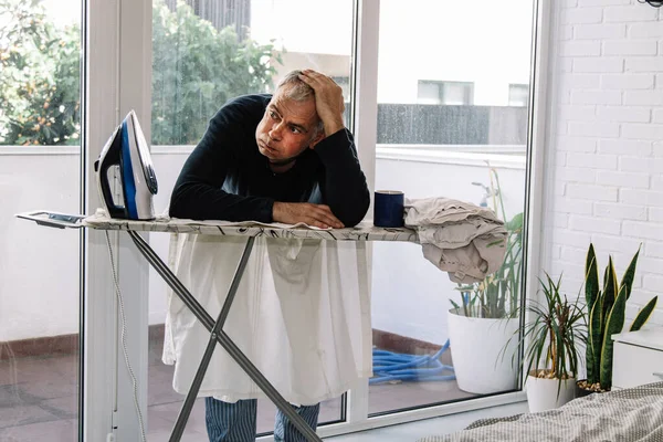 stressed overwhelmed man ironing at home with iron, concept equality in housework