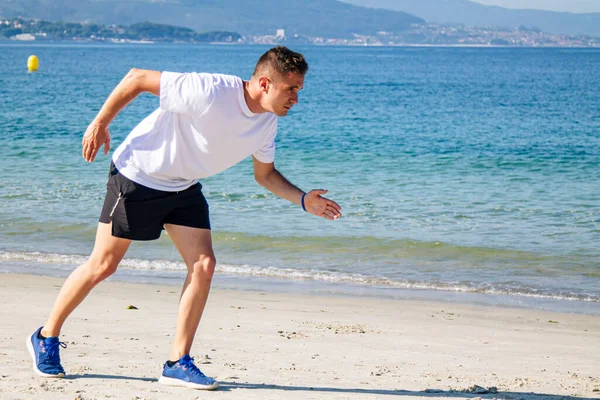 Genç adam sahilde koşmak için başlangıç pozisyonunda.