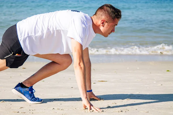 Genç adam sahilde koşmak için başlangıç pozisyonunda.