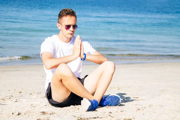 Kumsalda dinlenmek için yoga yapan bir adam.
