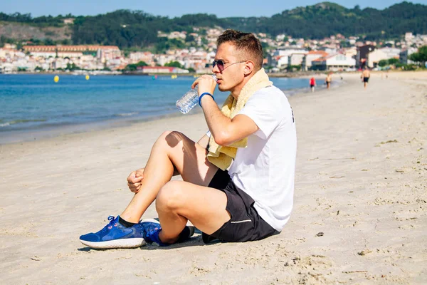 Sahilde dinlenen, içen ve koşudan sonra denize bakan bir adam.