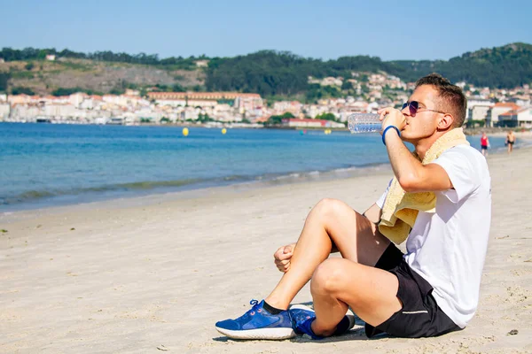 Sahilde dinlenen, içen ve koşudan sonra denize bakan bir adam.