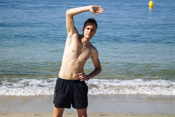Sahilde kol ve bacak egzersizi yapan bir adam.