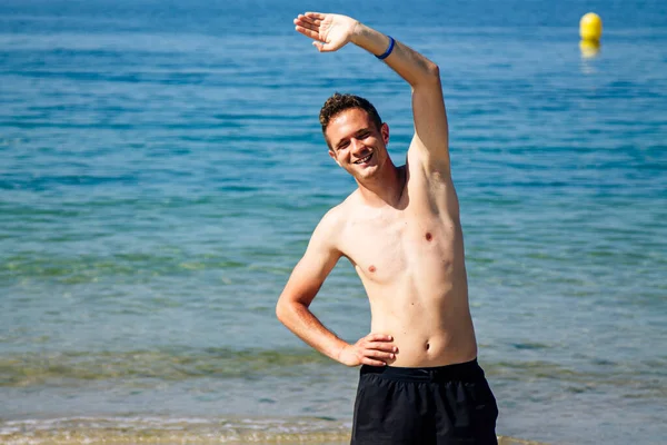 Sahilde kol ve bacak egzersizi yapan bir adam.