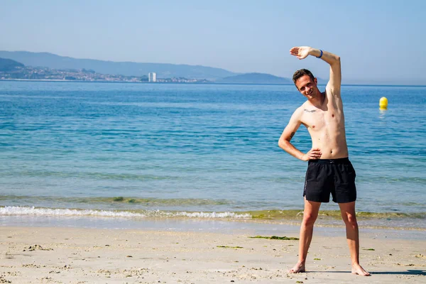 Sahilde kol ve bacak egzersizi yapan bir adam.