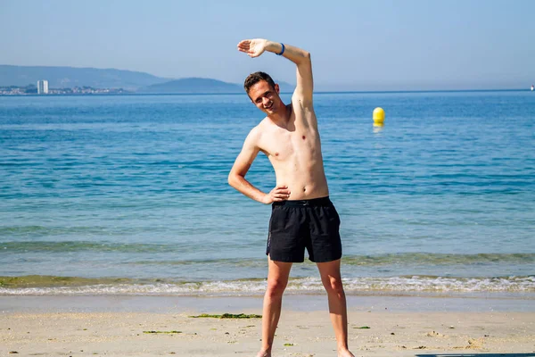 Sahilde kol ve bacak egzersizi yapan bir adam.