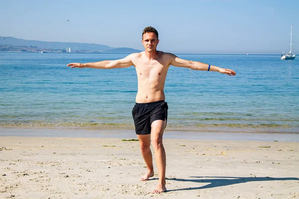 Genç adam plajda rahatlama egzersizleri yapıyor.