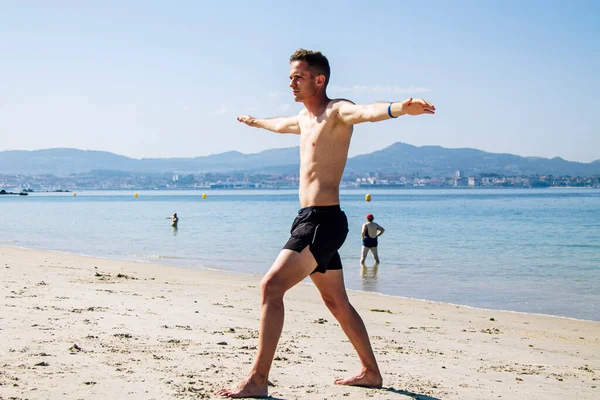 Genç adam plajda rahatlama egzersizleri yapıyor.