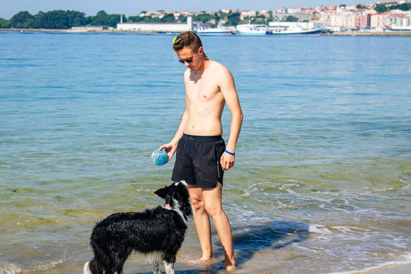 Sahilde evcil hayvanıyla oynayan bir adam.