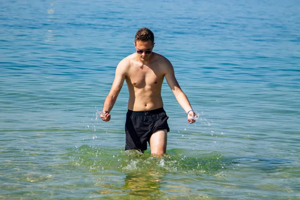 Yakışıklı genç adam sahilde okyanusta banyo yapıyor.