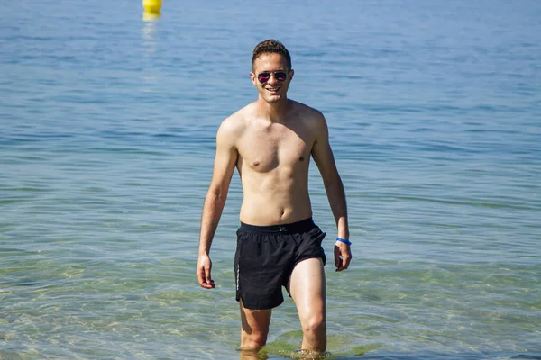 Yakışıklı genç adam sahilde okyanusta banyo yapıyor.