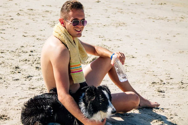 Genç bir adamın plajdaki portresi. Köpeğiyle dinleniyor ve içiyor.