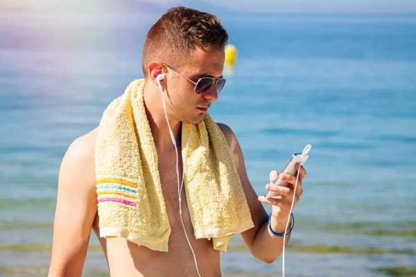Sahilde cep telefonu ve kulaklığı olan bir adam.