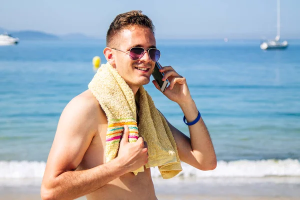 Genç adam plajda cep telefonuyla seyahat ediyor.