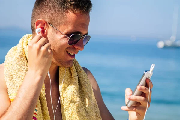 Sahildeki adam cep telefonu ve kulaklıklarla rahatladı.