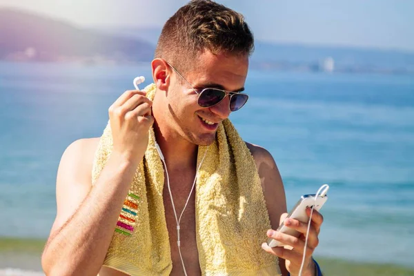 Sahilde cep telefonu ve kulaklığı olan bir adam.