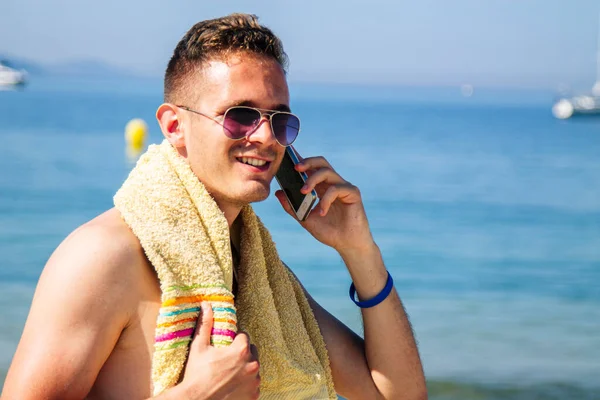 Genç adam plajda cep telefonuyla seyahat ediyor.