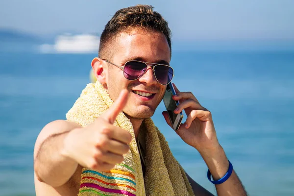 Sahilde seyahat ve otel rezervasyonları yapan genç bir adam. Arka planda yolcu gemisi var.