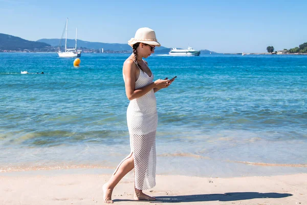 Plajda yürüyen bir kadın cep telefonu kullanıyor.