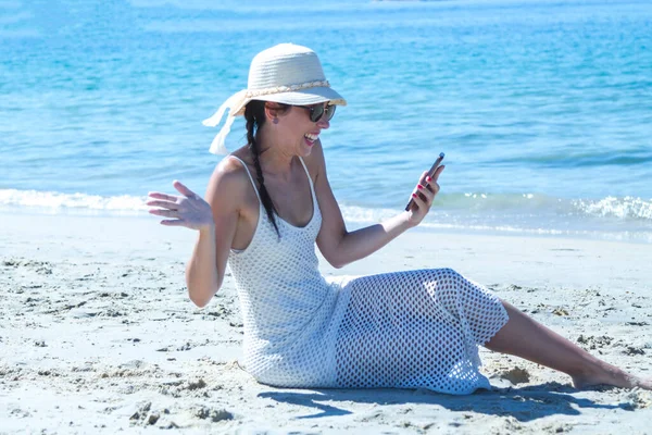 Sahilde cep telefonuyla sürpriz jestler yapan bir kadın.