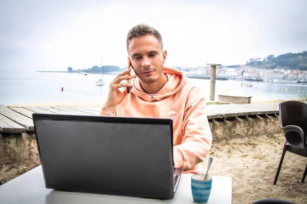 Dışarıda cep telefonu ve dizüstü bilgisayarı olan genç adam.