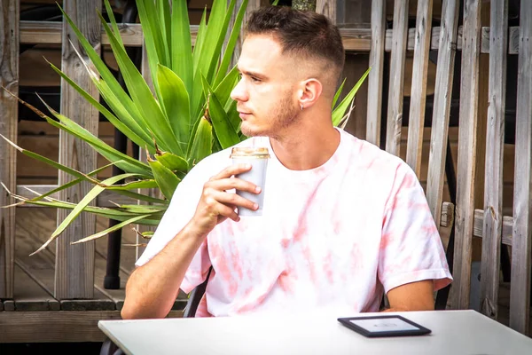 Genç adam dijital tablet kullanıyor ve açık bar terasında kahve içiyor.