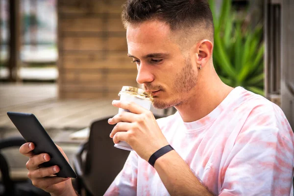 Adam dijital tablet ya da kitap kullanıyor ve dışarıda kahve içiyor.