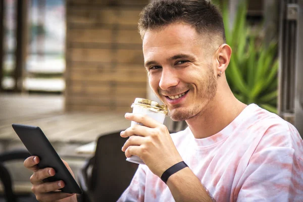 Adam dijital tablet ya da kitap kullanıyor ve dışarıda kahve içiyor.