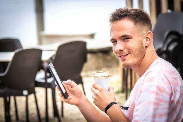 Adam dijital tablet ya da kitap kullanıyor ve dışarıda kahve içiyor.