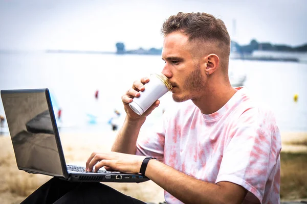 Genç adam dışarıda bilgisayarını kullanırken kahve içiyor.