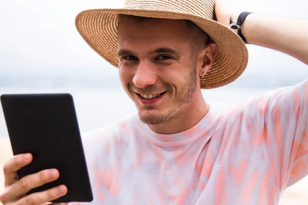 Şapkalı genç adam dışarıda dijital tablet kullanıyor.