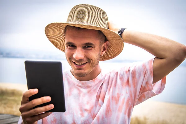 Şapkalı genç adam dışarıda dijital tablet kullanıyor.