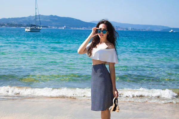 Kumsalda yürüyen şapkalı ve güneş gözlüklü bir kadın.