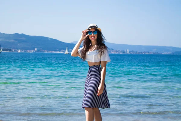 Kumsalda yürüyen şapkalı ve güneş gözlüklü bir kadın.