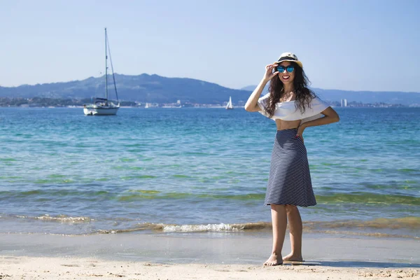 Kumsalda yürüyen şapkalı ve güneş gözlüklü bir kadın.