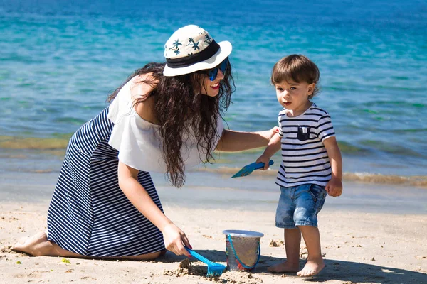 Anne ve küçük oğlu sahilde kova ve kürekle oynuyorlar.