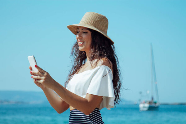 woman in hat by the beach checking mobile phone