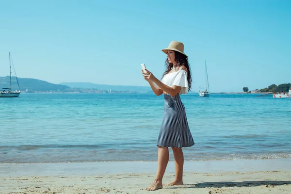 Kumsalda selfie çeken şapkalı bir kadın.
