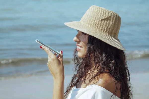 Plajda şapkalı bir kadın cep telefonuyla mesaj yolluyor.