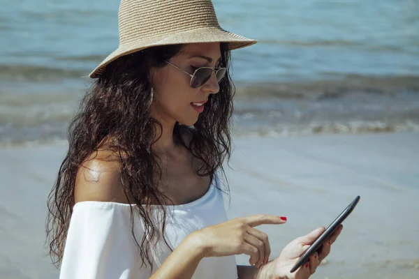Sahilde dijital tablet ya da e-kitap kullanan genç bir kadın.