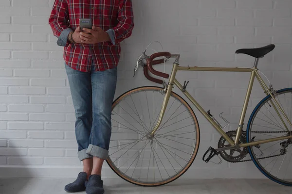 Evdeki adam bisikletin yanındaki duvara yaslanmış cep telefonuyla fotokopi çekiyor.