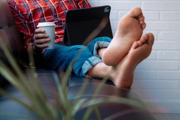 Dijital tabletli ve kanepede oturan hippi adam.