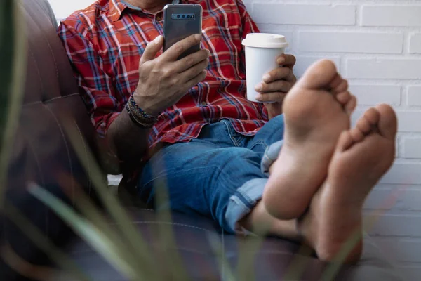 Kanepede uzanmış cep telefonu ve kahve olan hippi adam.