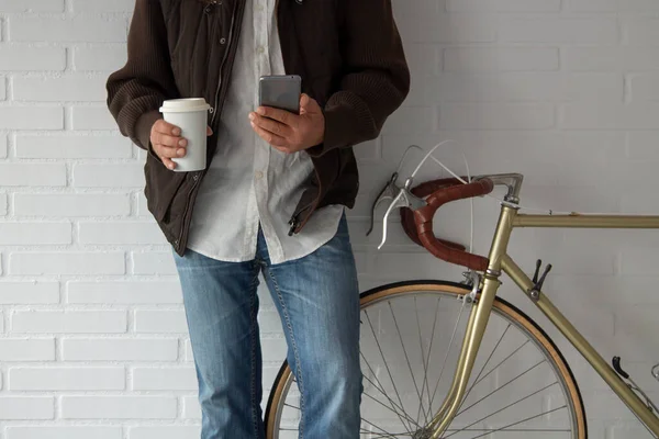 Bisikletin yanında ceketli ve cep telefonlu bir adam fotokopi alanı olan bir kahve içiyor.