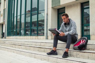 Enstitü veya üniversitenin önünde oturan kulaklıklı genç bir öğrenci