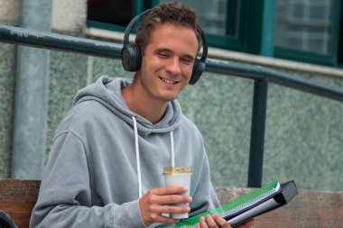 Üniversitede ya da üniversitede kulaklık takmış içki içen bir öğrenci.