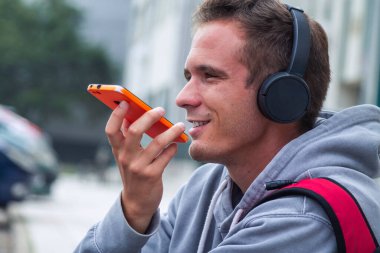 Sırt çantalı, kulaklık takan ve cep telefonuyla konuşan genç bir çocuk.