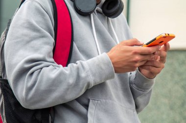 Sırt çantalı, kulaklık takan ve cep telefonu kullanan bir çocuk.